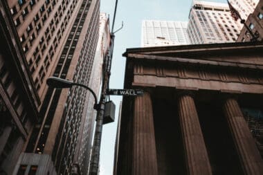 A low-angle shot capturing the Wall Street sign alongside towering business and financial buildings in New York City