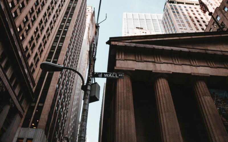 A low-angle shot capturing the Wall Street sign alongside towering business and financial buildings in New York City