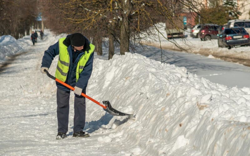 A man clears snow from the road with a shovel