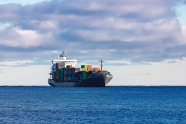 A modern gray cargo ship gliding smoothly across calm waters