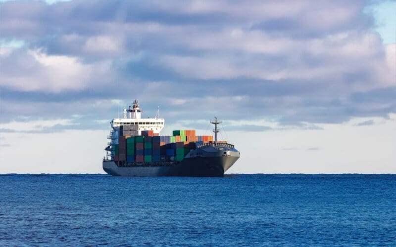 A modern gray cargo ship gliding smoothly across calm waters