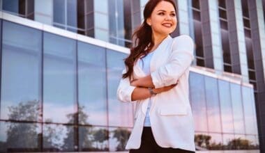 A portrait of a cheerful and successful businesswoman with a glass building in the background