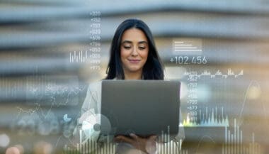 A self-assured young professional woman working on a laptop, with vibrant financial and data job charts superimposed in the background