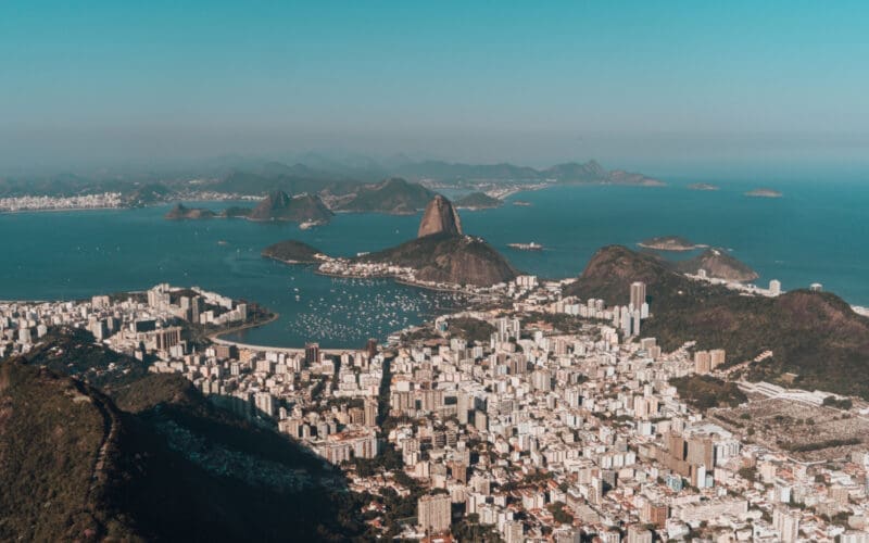 Aerial view of Rio de Janeiro, nestled between lush hills and the ocean, all beneath a clear blue sky