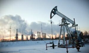 An oil pump stands against an industrial landscape, set against a winter sky filled with smoke