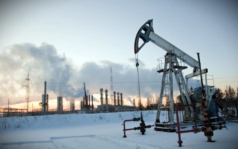 An oil pump stands against an industrial landscape, set against a winter sky filled with smoke