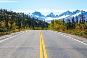 Asphalt road featuring yellow lines, set against the backdrop of Worthington Glacier in Alaska