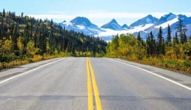 Asphalt road featuring yellow lines, set against the backdrop of Worthington Glacier in Alaska