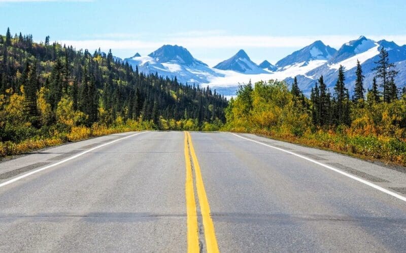 Asphalt road featuring yellow lines, set against the backdrop of Worthington Glacier in Alaska