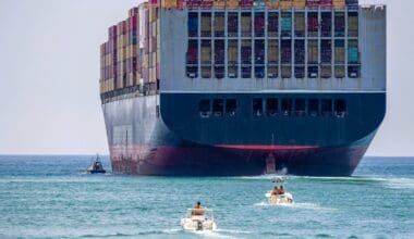 Container ship close to shore, accompanied by a tugboat and smaller vessels