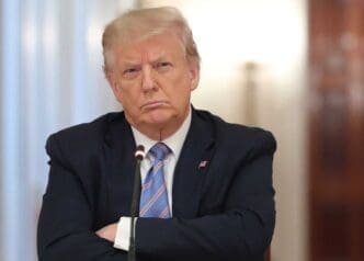 A serious Donald Trump looks straight ahead, with his arms crossed on a table