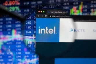 The Intel logo on a website is seen through a magnifying glass, with a blurry stock market chart in the background.