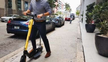 Modern executive man using Bolt, dockless electric scooter, in the streets of Brickell (Miami) with a Porsche behind him