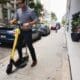 Modern executive man using Bolt, dockless electric scooter, in the streets of Brickell (Miami) with a Porsche behind him