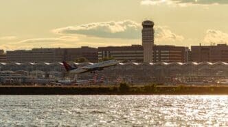Panoramic view of Ronald Reagan National Airport across Potomac River at sunset. image features the tower, terminals, parked planes and a Delta Airline plane taking off