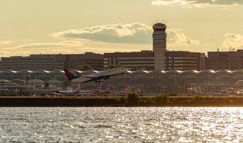 Panoramic view of Ronald Reagan National Airport across Potomac River at sunset. image features the tower, terminals, parked planes and a Delta Airline plane taking off
