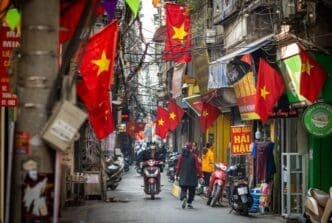 People go about daily life under Vietnamese flags in a narrow residential alleyway called Kham Thien Market in Hanoi, Vietnam