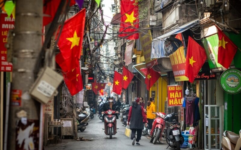 People go about daily life under Vietnamese flags in a narrow residential alleyway called Kham Thien Market in Hanoi, Vietnam