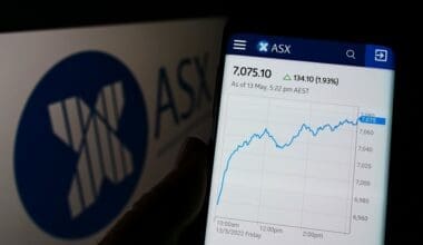 Person holding cellphone with webpage of Australian Securities Exchange Ltd (ASX) on screen in front of logo. Focus on center of phone display