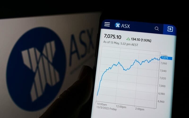 Person holding cellphone with webpage of Australian Securities Exchange Ltd (ASX) on screen in front of logo. Focus on center of phone display