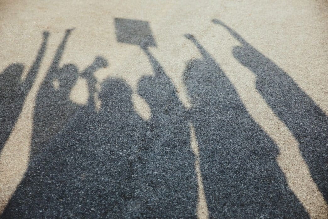 Shadows cast over the asphalt as people of various ages and races gather on the street to protest for equal rights