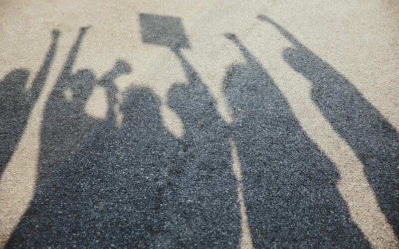 Shadows cast over the asphalt as people of various ages and races gather on the street to protest for equal rights