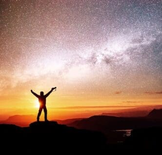 Silhouette of a dreamer standing on top of mountain and pointing to The Milky Way before sunrise and enjoying with colorful night sky