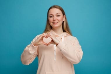 Smiling young blonde woman making a love sign that symbolizes a healthy heart