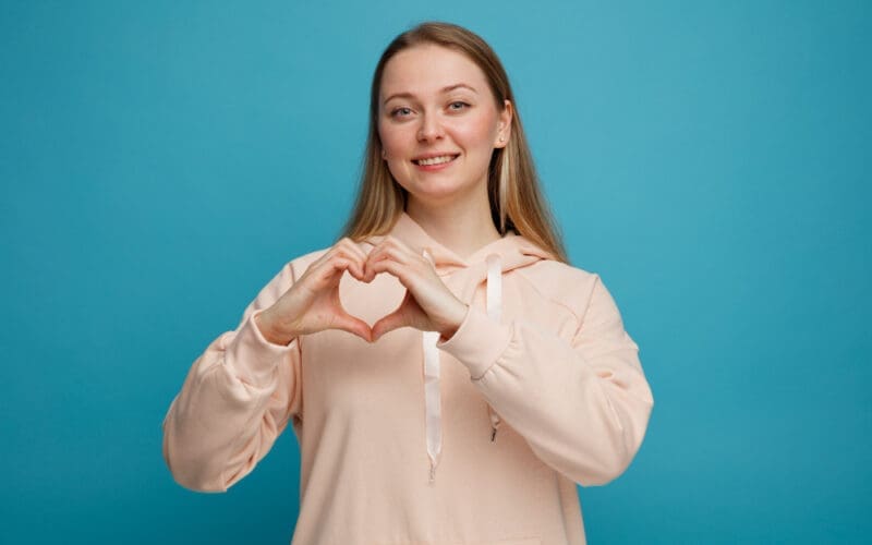 Smiling young blonde woman making a love sign that symbolizes a healthy heart