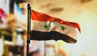 Syria's flag in the foreground with a blurred cityscape background at sunrise