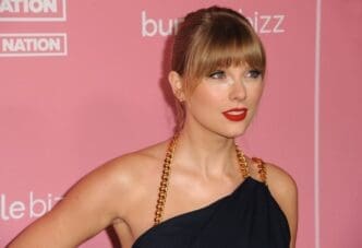 A close-up portrait of Taylor Swift with her hair in an updo and bold red lipstick