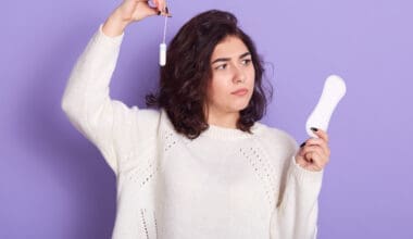 Thoughtful dark-haired woman contemplating the choice between tampons and sanitary napkins