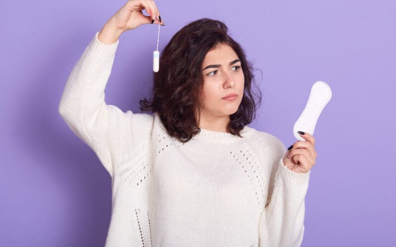 Thoughtful dark-haired woman contemplating the choice between tampons and sanitary napkins