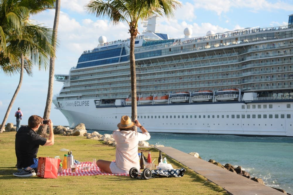 Tourists having a picnic at South Pointe Park, Miami Beach, taking photos of a large cruise ship passing by.