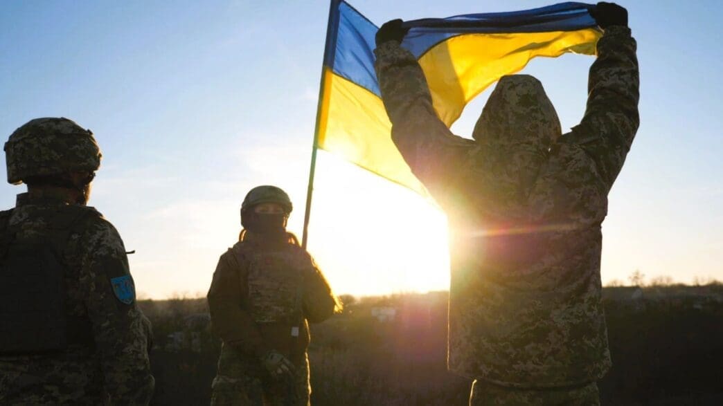 Ukrainian soldiers stand on a hill, proudly raising the national flag as a symbol of victory over Russian aggression