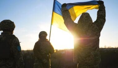 Ukrainian soldiers stand on a hill, proudly raising the national flag as a symbol of victory over Russian aggression