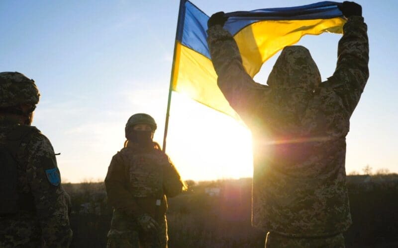 Ukrainian soldiers stand on a hill, proudly raising the national flag as a symbol of victory over Russian aggression