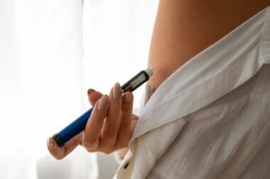 A woman independently administering weight loss medication, such as Ozempic, from a sideways perspective