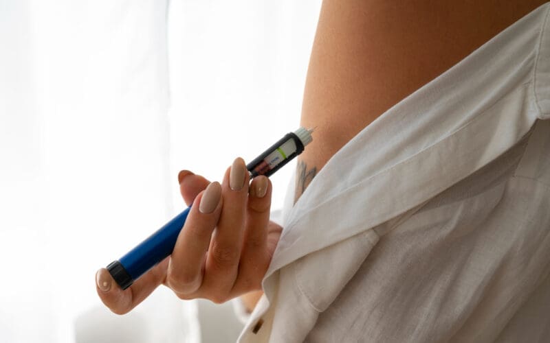 A woman independently administering weight loss medication, such as Ozempic, from a sideways perspective