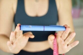 A girl in sportswear is holding an Ozempic insulin pen and a tape measure to measure her waist. By Shutterstock - Pietukhova