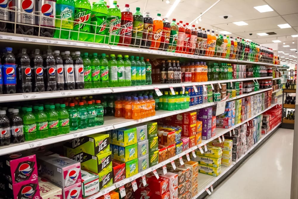 A view of the soda aisle of a grocery store, featuring several brands and colors of carbonated beverages