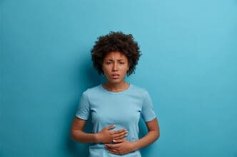 An Afro woman experiences discomfort in her stomach, placing her palms gently on her abdomen.
