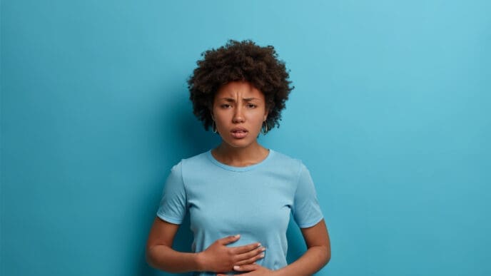 An Afro woman experiences discomfort in her stomach, placing her palms gently on her abdomen.