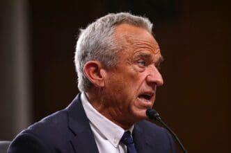 A close-up side-profile of Robert F. Kennedy Jr. speaking into a microphone