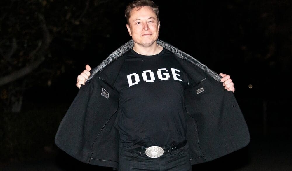 Elon Musk reveals a DOGE t-shirt and a Tesla belt buckle before entering the White House