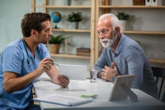 Male doctor using touchpad and explaining medical test results to his senior patient during medical appointment