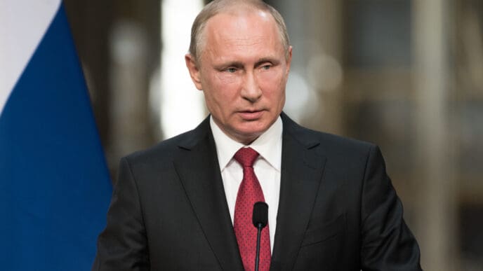A close-up portrait of Vladimir Putin, President of the Russian Federation, speaking at a press conference.