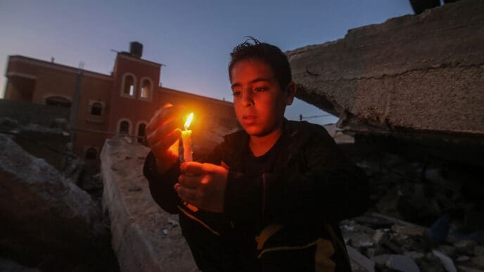 Palestinian children hold candles near buildings destroyed in Israeli air strikes in the southern Gaza Strip city of Rafah, on May 25, 2021