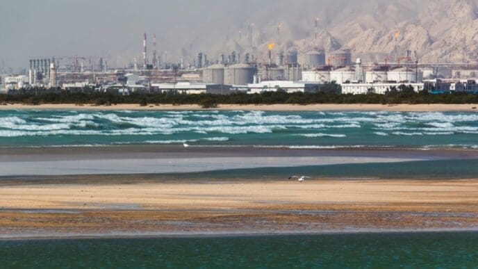 Seascape of blue waves and flying birds with a background of a refinery complex in southern province of Bushehr, Iran