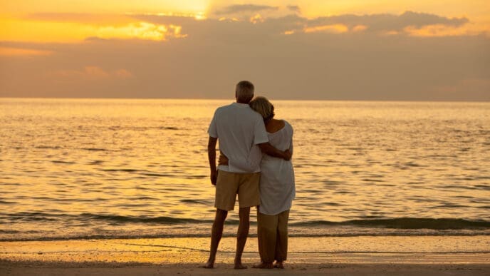 Senior man and woman couple embracing at sunset or sunrise on a deserted tropical beach